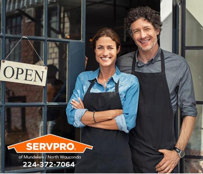 Happy business owners stand outside their store in front of an “open” sign.